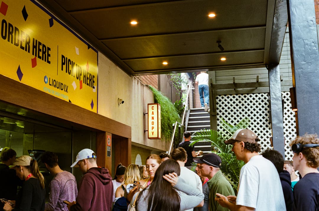 Crowd queuing under Liquid I.V. order here signage at The Golden Sheaf
